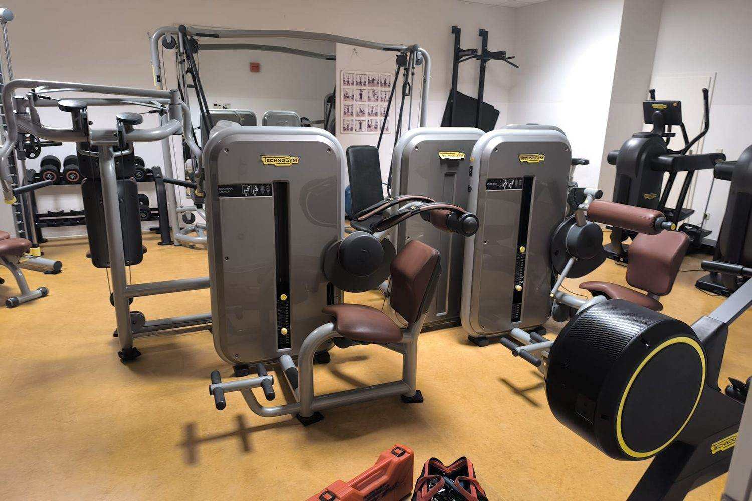 Ausgestatteter Trainingsraum mit Steckgewichtsgeräten, Kabelzug, Hantelablage und Crosstrainer