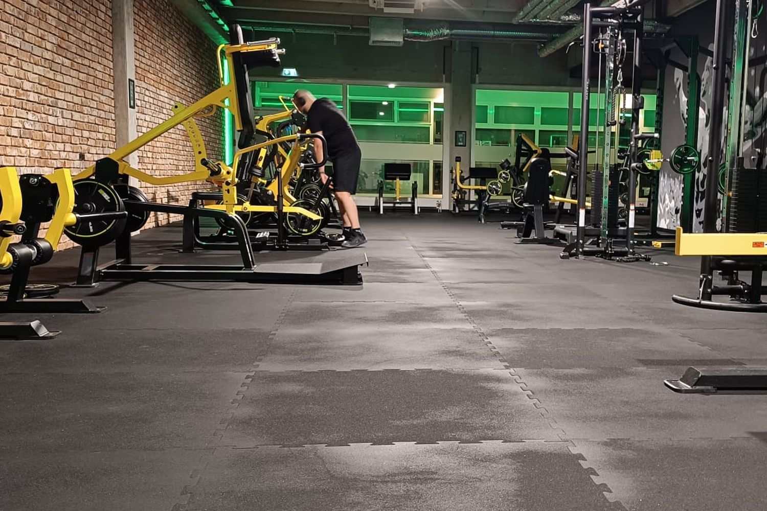 Clubfläche mit grüner Beleuchtung, plate-loaded Geräten und Racks, Techniker im Hintergrund