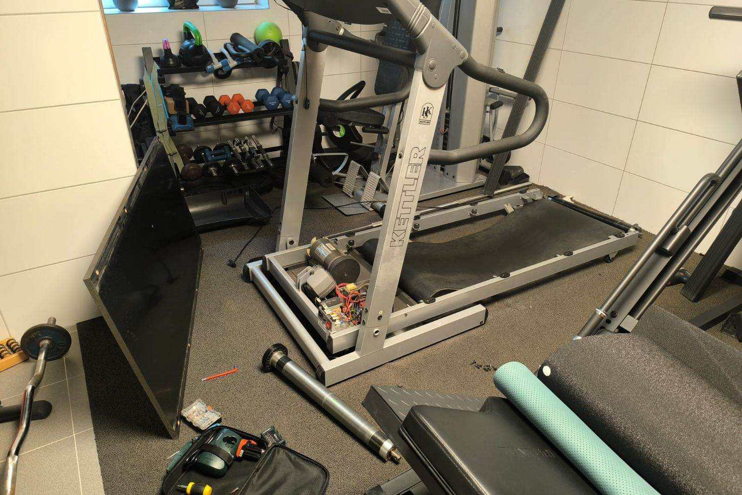 Laufband mit geöffnetem Motorraum bei der Reparatur, Antriebsmotor und ausgebaute Rolle sichtbar