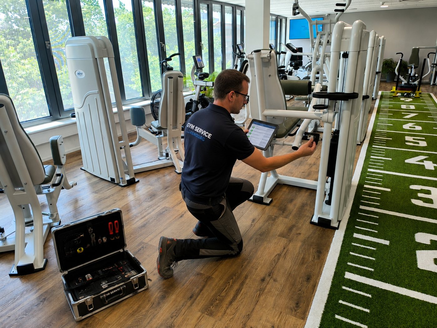 Gym Service technician filling in a maintenance checklist on a tablet beside a strength machine