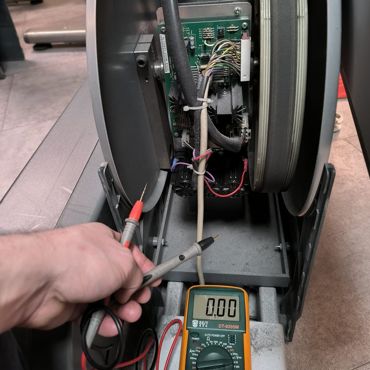 Technicien mesurant au multimètre sur l’électronique d’un vélo elliptique ouvert