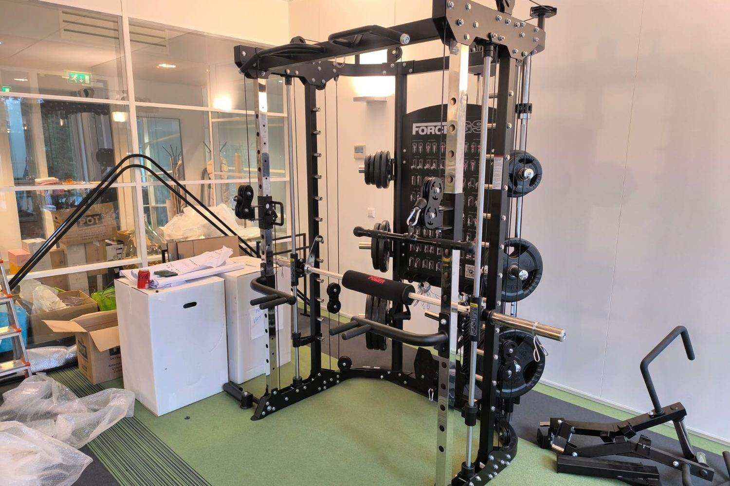 Station de musculation neuve montée, poulies et disques en place, emballages encore au sol