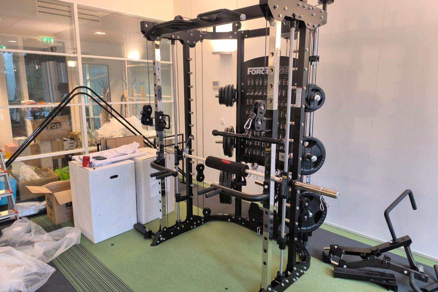 Newly assembled multi-gym with cable pulleys and weight plates, packaging still beside it