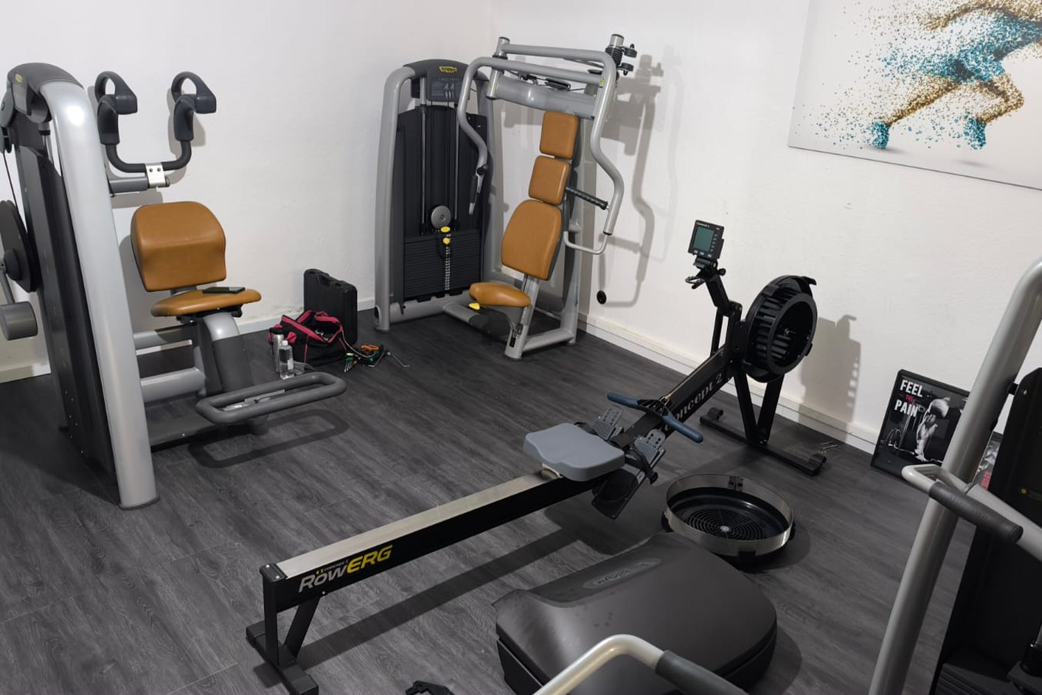 Salle avec appareils de musculation et de cardio, mallette à outils et sacoche de service posées au sol