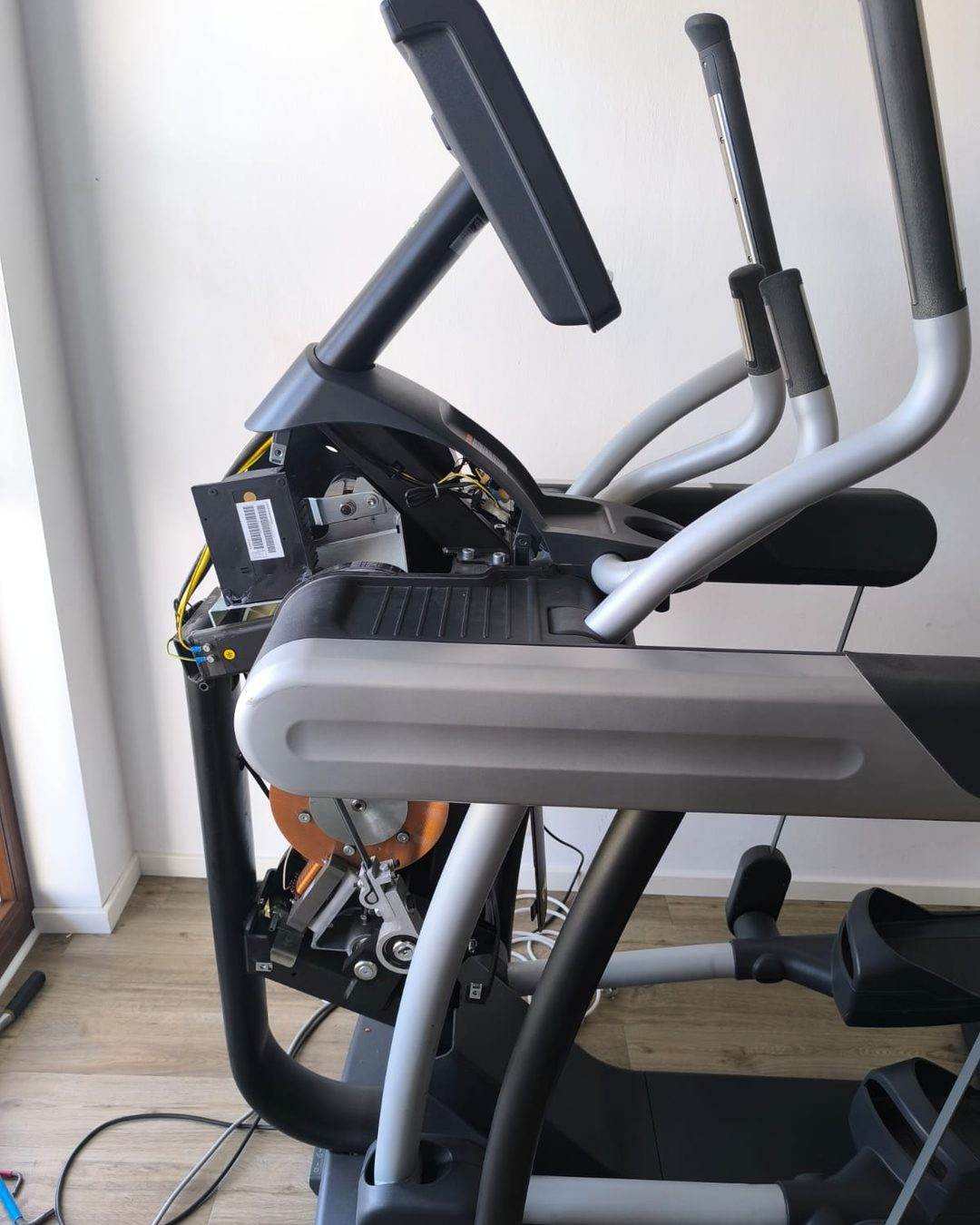 Vélo elliptique ouvert en cours de réparation : console démontée, électronique et entraînement visibles
