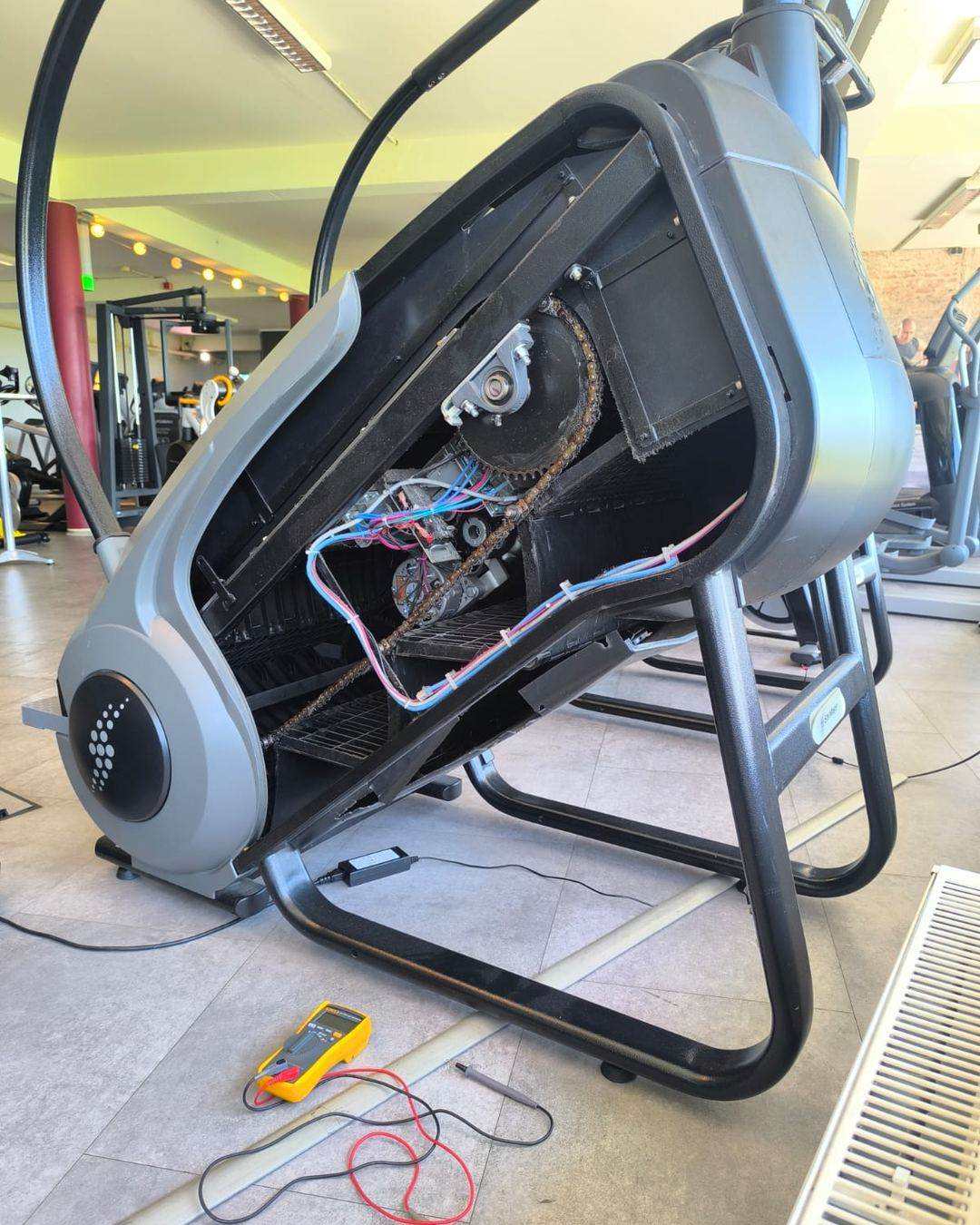 Simulateur d’escalier ouvert pour réparation : chaîne d’entraînement, moteur et faisceau électrique visibles