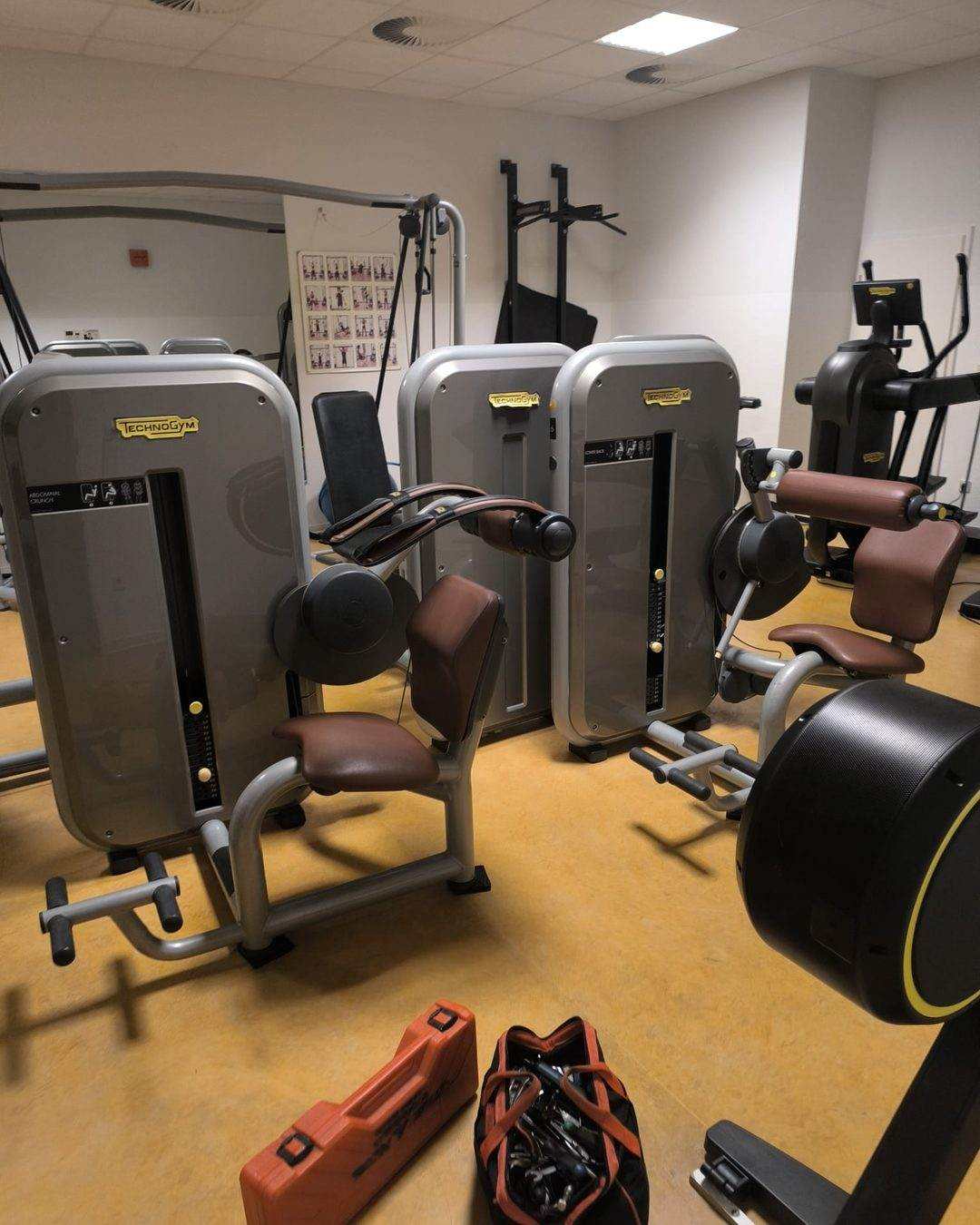 Salle équipée de machines de musculation à colonne de poids, caisse à outils et sacoche du technicien posées au sol