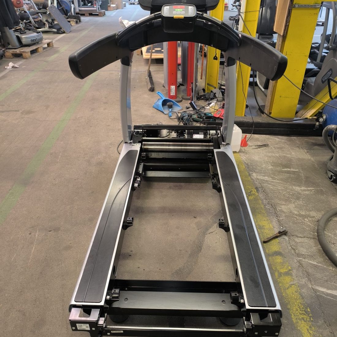 Tapis de course vu de face, plateau déposé, rouleaux avant et arrière accessibles