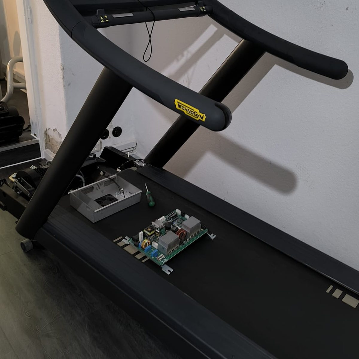 Tapis de course capot moteur retiré, carte électronique et bloc ventilateur posés sur la bande