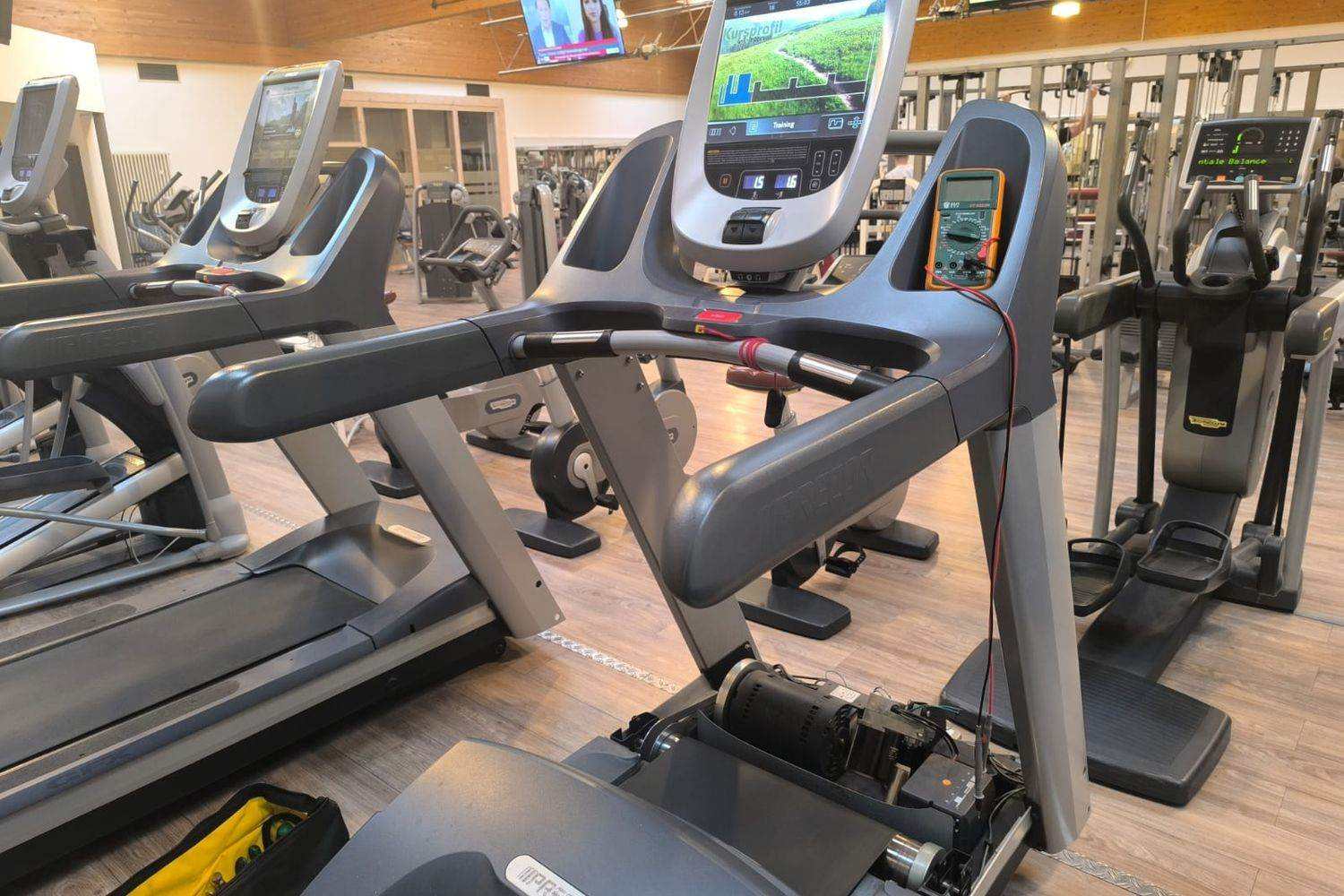 Multimeter clipped to the console of a club treadmill during an electrical measurement