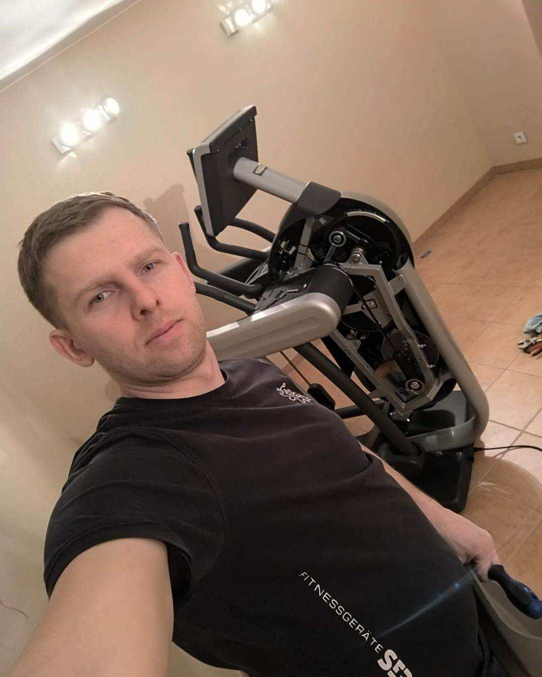 Techniker neben einem Crosstrainer mit abgenommener Antriebsverkleidung, Mechanik im Inneren sichtbar