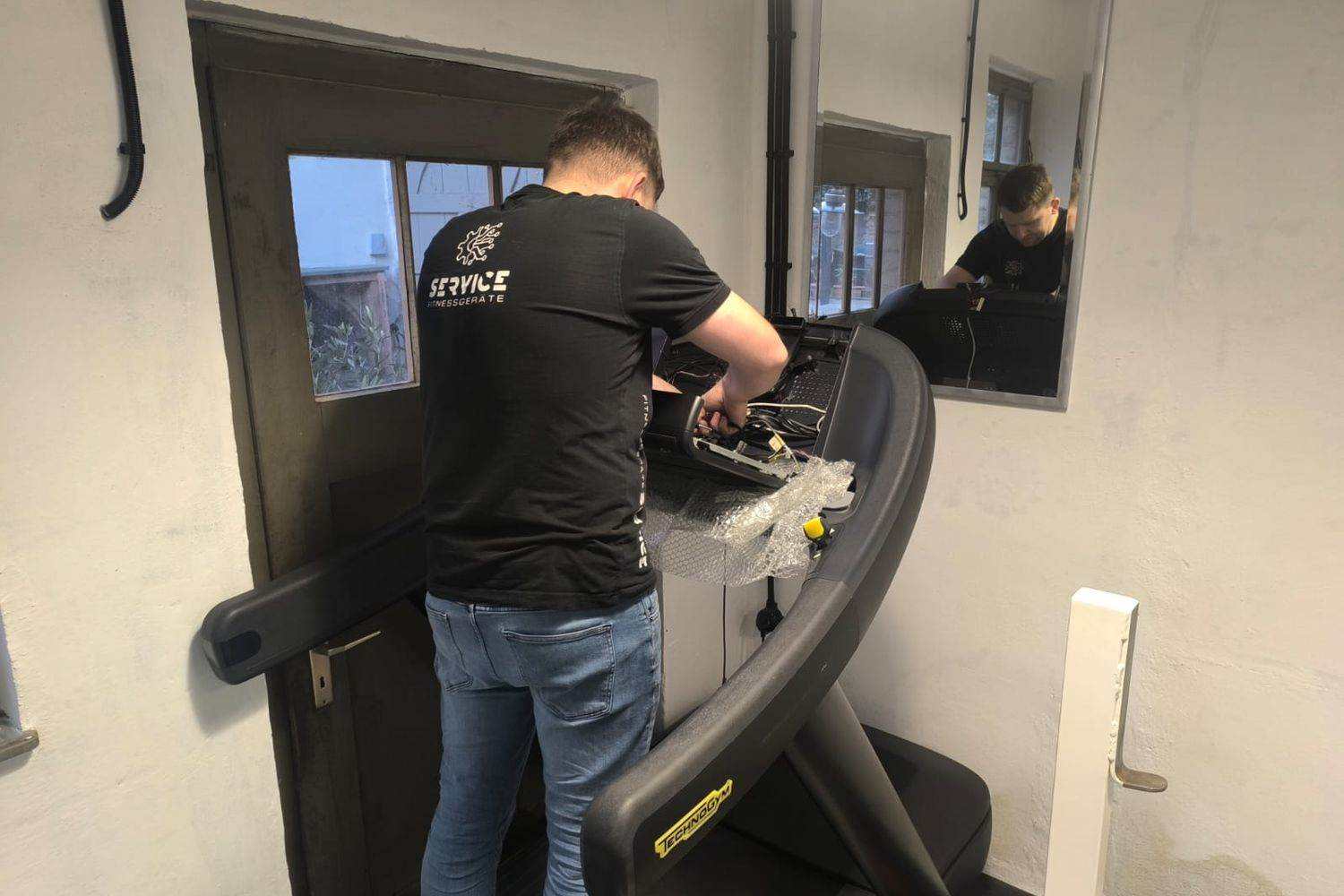 Techniker schafft un der opgemaachter Konsol vun engem Laafband mat oppener Verkabelung