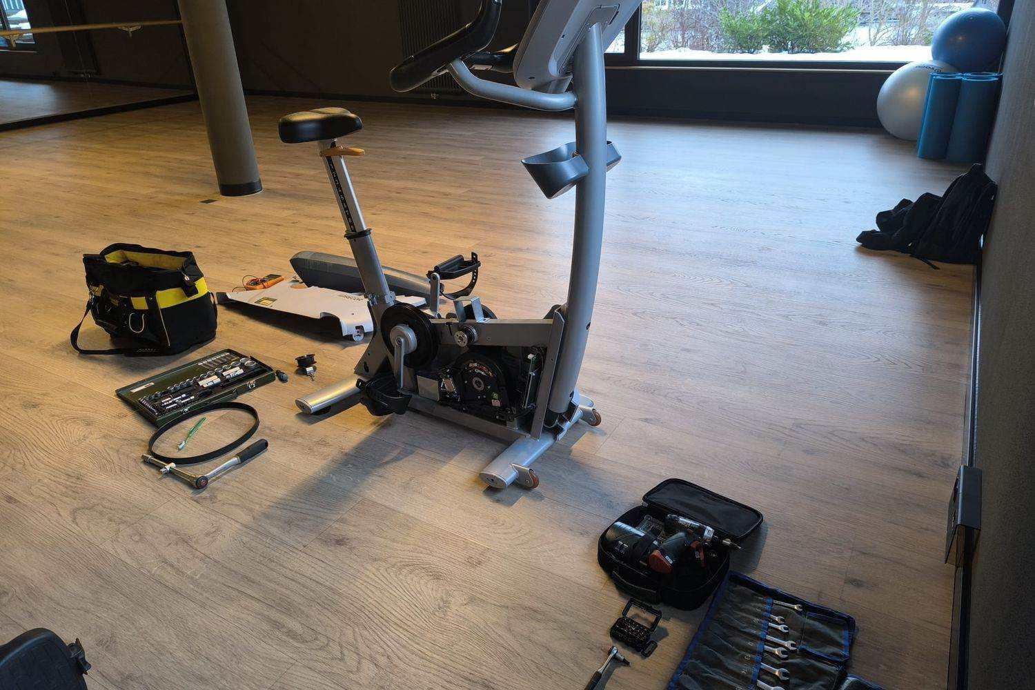 Exercise bike opened up with the tool kit laid out on the floor before the work starts: tool bag, socket set, torque wrench and drive belt