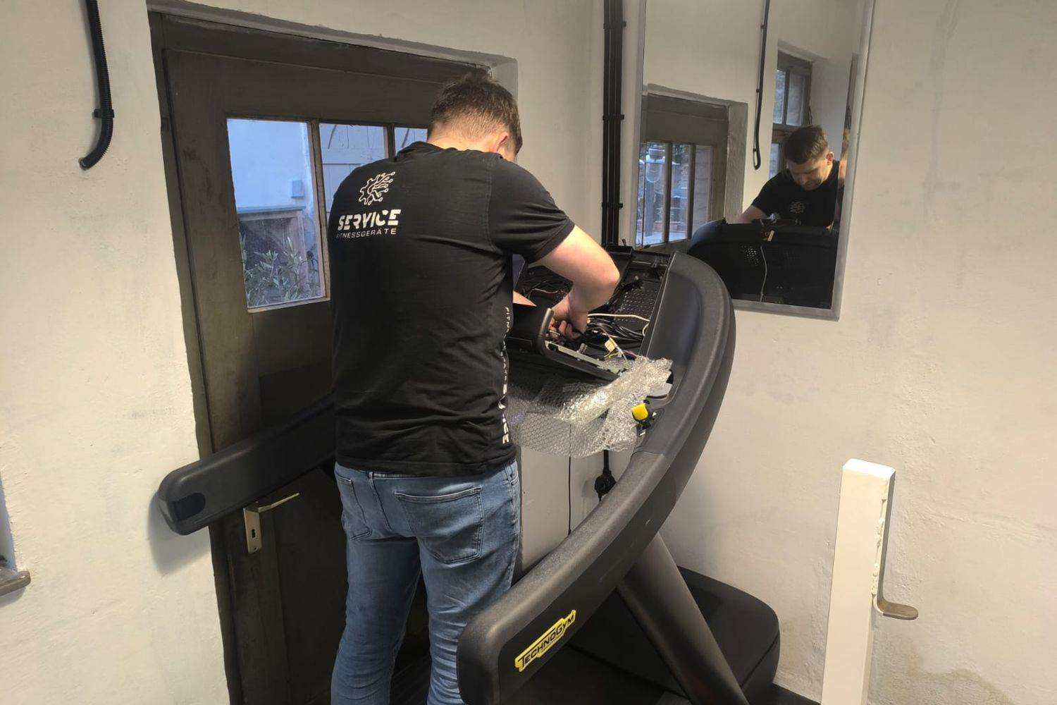 Technician working on the opened console of a treadmill with the wiring exposed