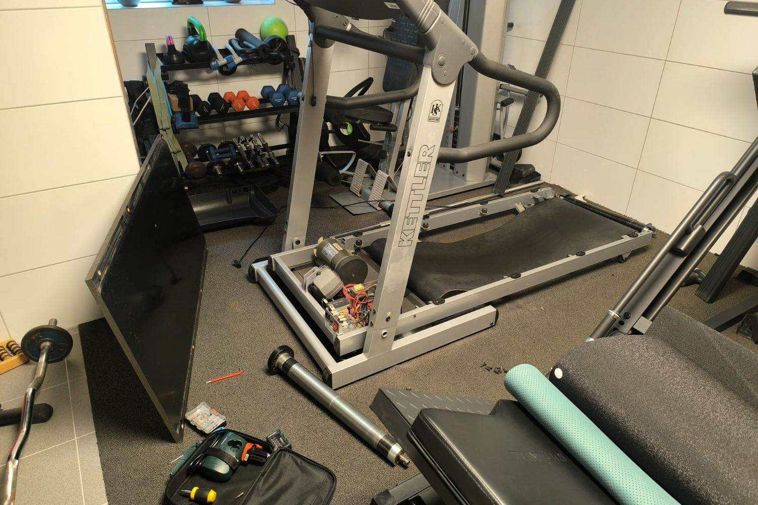 Treadmill with the motor housing open during repair, drive motor and a removed roller visible